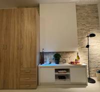 Vám ponúka garsonku vo VYHĽADÁVANEJ lokalite m - Interiér rekreačného apartmánu s podlahou s dreveným dekorom, skriňou a štýlovou lampou.