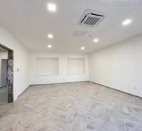 Vám ponúka  na predaj budovu na BÝVANIE aj PODN - Interiér priestrannej miestnosti s drevenou podlahou a zabudovaným osvetlením. Budova má bielu stenu.