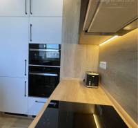 Vám ponúka na Prenájom 2-izbový byt s loggiou  - Kuchyňa v 2-izbovom byte s bielymi skrinkami a podlahou s dreveným dekorom.