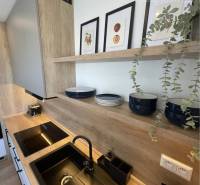 Vám ponúka na Prenájom 2-izbový byt s loggiou  - Kuchyňa v 2-izbovom byte s dreveným dekorom, čierny drez a dekoračné obrázky.