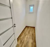 Vám ponúka modernú 4-izbovú novostavbu v Dunajs - Úzka chodba s bielymi stenami v rodinnom dome, podlaha s dreveným dekorom.