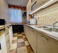 Vám ponúka 3-izbový byt s loggiou po kompletnej - Kuchyňa v 3-izbovom byte s podlahou s dreveným dekorom a svetlými skrinkami.