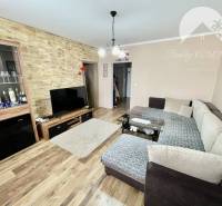 Vám ponúka 3-izbový byt s loggiou po kompletnej - Obývačka v 3-izbovom byte s podlahou s dreveným dekorom a rohovou sedačkou.