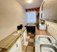 Vám ponúka 3-izbový byt s loggiou po kompletnej - Kuchyňa v 3-izbovom byte s dlažbou a dreveným dekorom na skrinkách.