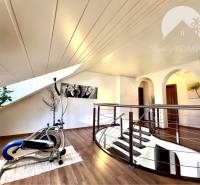 Ponúka na PREDAJ zrekonštruovaný 5 izbový podpi - Interiér rodinného domu s cvičebným strojom, schodisko a dekorácie na stene.