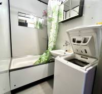 Ponúka na PREDAJ 1 izbový byt v Komárne - Kúpeľňa so sprchovacím kútom a práčkou v 1-izbovom byte s bielymi stenami.