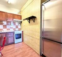 Ponúka na PREDAJ 1 izbový byt v Komárne - Kuchyňa 1-izbového bytu s podlahou s dreveným dekorom a nerezovou chladničkou.