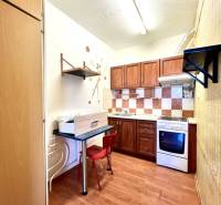 Ponúka na PREDAJ 1 izbový byt v Komárne - Kuchyňa v 1-izbovom byte s podlahou s dreveným dekorom a plynovým sporákom.