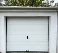 Vám ponúka na PREDAJ zrekonštruovanú garáž v Du - Garáže na Nevädzovej ulici v Dunajskej Strede s bielymi dverami a stromami v pozadí.