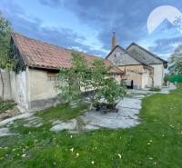 Investičný pozemok s obývateľným domom vo Vrakúni - Rodinný dom vo Vrakúni s trávnikom, stromami a prístavbou pod zamračenou oblohou.