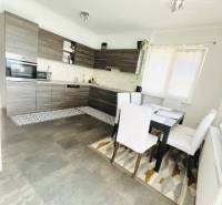 Vám ponuka na predaj útulný 3-izbový rodinný d - Kuchyňa v rodinnom dome s podlahou s dreveným dekorom, jedálenským stolom a veľkým oknom.