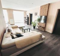 Vám ponuka na predaj útulný 3-izbový rodinný d - Obývacia izba v rodinnom dome s veľkou sedačkou a podlahou s dreveným dekorom.