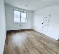 Vám ponúka na predaj moderný 4-izbový bungalov - Izba s bielymi stenami a podlahou s dreveným dekorom v rodinnom dome.