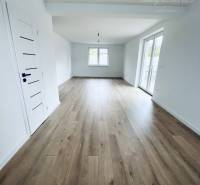 Vám ponúka na predaj moderný 4-izbový bungalov - Interiér rodinného domu s bielymi stenami a podlahou s dreveným dekorom.