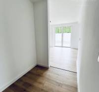 Vám ponúka na predaj moderný 4-izbový bungalov - Interiér rodinného domu s podlahou s dreveným dekorom a bielymi stenami.