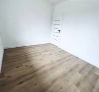 Vám ponúka na predaj moderný 4-izbový bungalov - Izba v rodinnom dome s bielymi stenami a podlahou s dreveným dekorom.