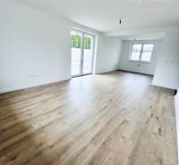 Vám ponúka na predaj moderný 4-izbový bungalov - Obývacia izba v rodinnom dome s podlahou s dreveným dekorom a veľkými oknami.