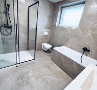 Vám ponúka na predaj moderný 4-izbový bungalov - Kúpeľňa v rodinnom dome s presklenným sprchovým kútom a svetlými obkladmi.