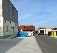 Autoservis s výbavou pre vozidlá v uzavretom priemyselnom areáli - HC - Budova v Hlohovci s kontajnerom a zaparkovaným autom na ulici.