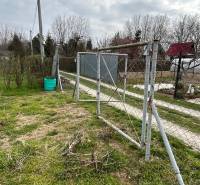 PREDAJ - Záhradka v Šali za klziskom   - Záhrada v Šali s jednoduchou bránkou a sieťovaným plotom na vidieku.