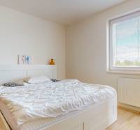 4i byt s terasou a parkovaním v tichej časti Rovinky | 89m2 - Svetlá spálňa s posteľou, dekoráciou na stene a podlahou s dreveným dekorom v 4-izbovom byte.