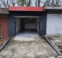 Garáž Púpavova, Karlova Ves + pivnica - Garáž na ulici Púpavová obklopená stromami, betónová dlažba a otvorené dvere.