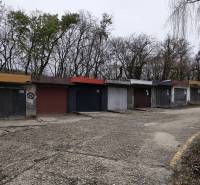 Garáž Púpavova, Karlova Ves + pivnica - Staršie garáže pri Púpavovej ulici, pokryté stromami a prázdnou cestou.