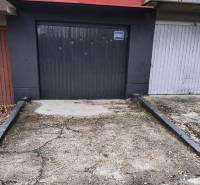 Garáž Púpavova, Karlova Ves + pivnica - Sivá garáž na ulici Púpavová, obklopená stromami, príjazdová cesta pred garážou.