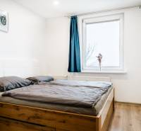 Útulný 2-izbový byt na prenájom - Spálňa s podlahou s dreveným dekorom a posteľou v 2-izbovom byte, modrý záves na okne.