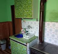 Na predaj rodinný dom Kosihovce - Staršia kuchyňa v rodinnom dome s kachľami, umývadlom a dekoratívnym obložením.