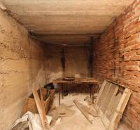 Dom s veľkým pozemkom 3099m2, Melčice-Lieskové - Starý skladový priestor s tehlovou stenou obsahuje stôl, drevené dosky a odpadový materiál.