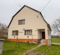 Dom s veľkým pozemkom 3099m2, Melčice-Lieskové - Rodinný dom s dvomi oknami, záhrada so stromami a satelitná anténa.