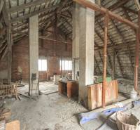 Dom s veľkým pozemkom 3099m2, Melčice-Lieskové - Podkrovný priestor prerábky rodinného domu so strešnými trámami a tehálovou stenou.
