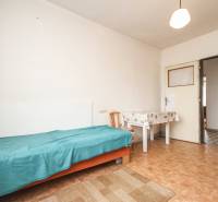 Dom s veľkým pozemkom 3099m2, Melčice-Lieskové - Izba v rodinnom dome s posteľou, stolom, stoličkou, dverami a jednoduchým podlahovým kobercom.