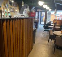 Reštaurácia na predaj v centre Košíc na Hlavnej 74 - Interiér gastro priestorov s dreveným barom a stolmi. Vidieť aj dekoratívne osvetlenie.