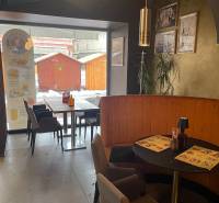 Reštaurácia na predaj v centre Košíc na Hlavnej 74 - Gastro priestory s kaviarenským sedením, dekoráciami na stenách a výhľadom na drevené stánky vonku.