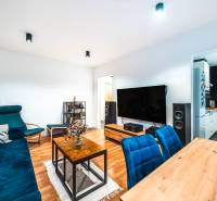 Na prenájom moderný 2-izbový byt  - Obývacia izba 2-izbového bytu s podlahou s dreveným dekorom a modrými sedacimi súpravami.