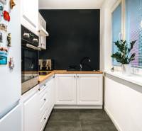 Na prenájom moderný 2-izbový byt  - Kuchyňa v 2-izbovom byte s čiernou stenou, dreveným dekorom a bielymi skrinkami.