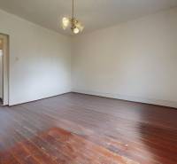 Veľký priestranný pozemok o rozlohe 7445 m2 s RD, Jelka  - Prázdna izba s drevenou podlahou, lustrom a vstupnými dverami v rodinnom dome.