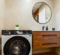 NOVOSTAVBA | 2i Mezonet + 1i štúdio s terasou a parkingom v CENTRE PO - Kúpeľňa v 1-izbovom byte s práčkou, kruhovým zrkadlom a skrinkou.