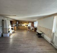 Skrytý raj v srdci prírody - Interiér rodinného domu s kuchynským kútom, murovanou pecou a podlahou s dreveným dekorom.