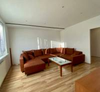 Pekný 3 izbový byt s lodžiou, ulica Nad Lúčkami, BA IV. Karlova Ves - Obývačka v 3-izbovom byte s rohovou sedačkou, stôl a podlaha s dreveným dekorom.