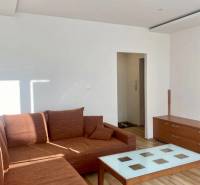 Pekný 3 izbový byt s lodžiou, ulica Nad Lúčkami, BA IV. Karlova Ves - Obývacia izba s hnedou sedačkou a stolíkom, 3-izbový byt s podlahou s dreveným dekorom.