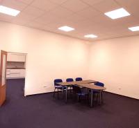 Na prenájom priestor- kancelária 60 m2 Trnava - Františkánska - Kancelária s modrými stoličkami a stolmi, biela stena, otvorené dvere k malej kuchynke.