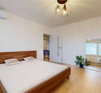 Kvalitne rekonštruovaný byt vo výbornej lokalite Petržalky - Spálňa v 3-izbovom byte s posteľou, zrkadlom a podlahou s dreveným dekorom.