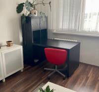 NA PRENÁJOM ÚTULNÝ 1-IZBOVÝ BYT, ČIASTOČNÁ REK., KAROLA ADLERA, BA - Pracovný kút v 1-izbovom byte s čiernym stolom, červenou stoličkou a podlahou s dreveným dekorom.