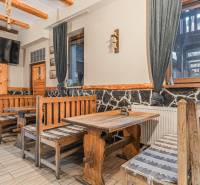 Predaj Exkluzívna ponuka elegantného penziónu s hostincom - Interiér z Hotely a penzióny s rustikálnymi drevenými lavicami a stolom, dekoratívny kameň na stene.