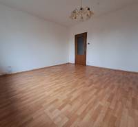 REZERVOVANÉ 2-izbový byt s nádherným výhľadom v pôvodnom stave   - Izba v 2-izbovom byte s podlahou s dreveným dekorom a lustrom.