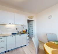 ZREKONŠTRUOVANÝ 3-IZBOVÝ BYT (74 m2) S BALKÓNOM, PIVNICOU, 2 x WC - Kuchyňa v 3-izbovom byte s podlahou s dreveným dekorom, jedálenským stolom a bielymi skrinkami.