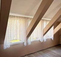 Na predaj unikátna dvojpodlažná budova na podnikanie aj bývanie - Interiér podkrovia s oknami a podlahou s dreveným dekorom.